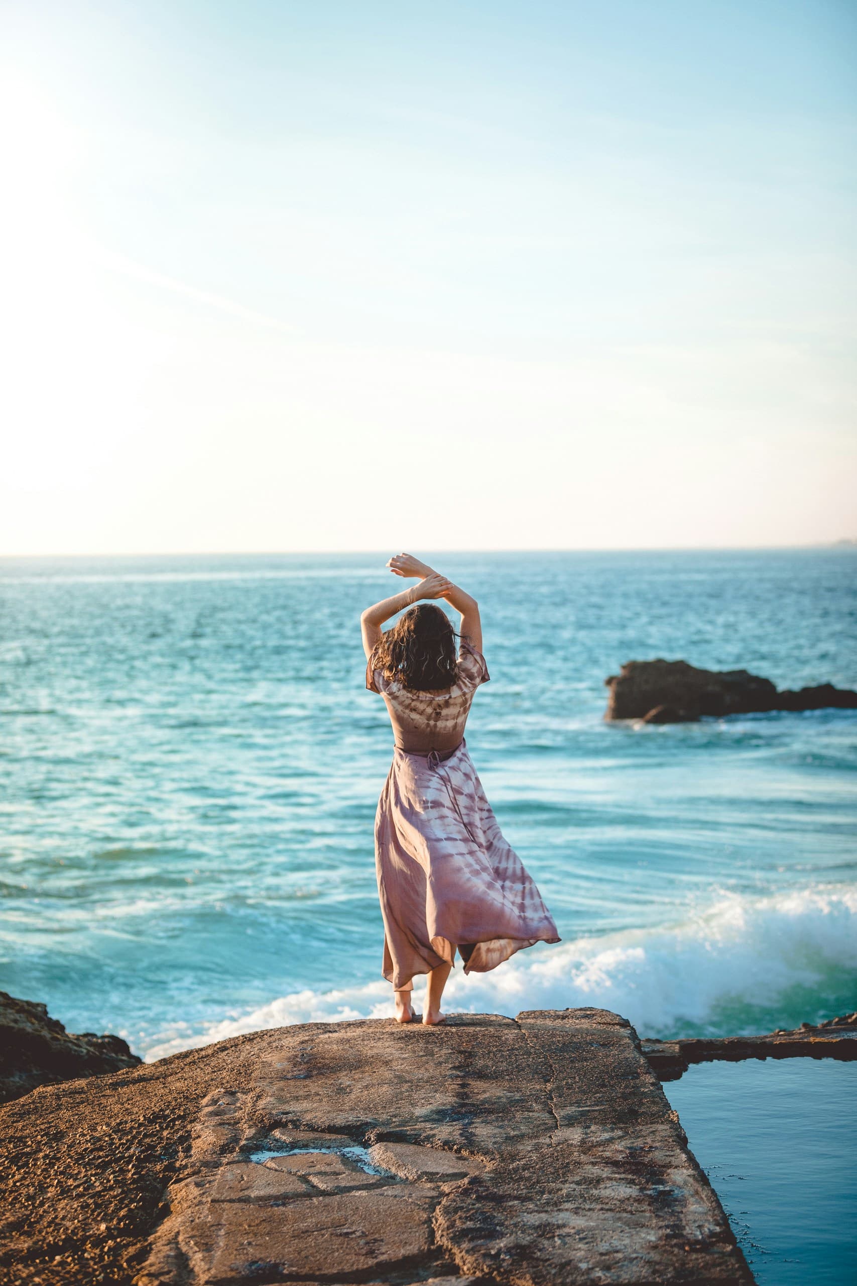 Mujer al borde del acantilado mirando el mar al amanecer