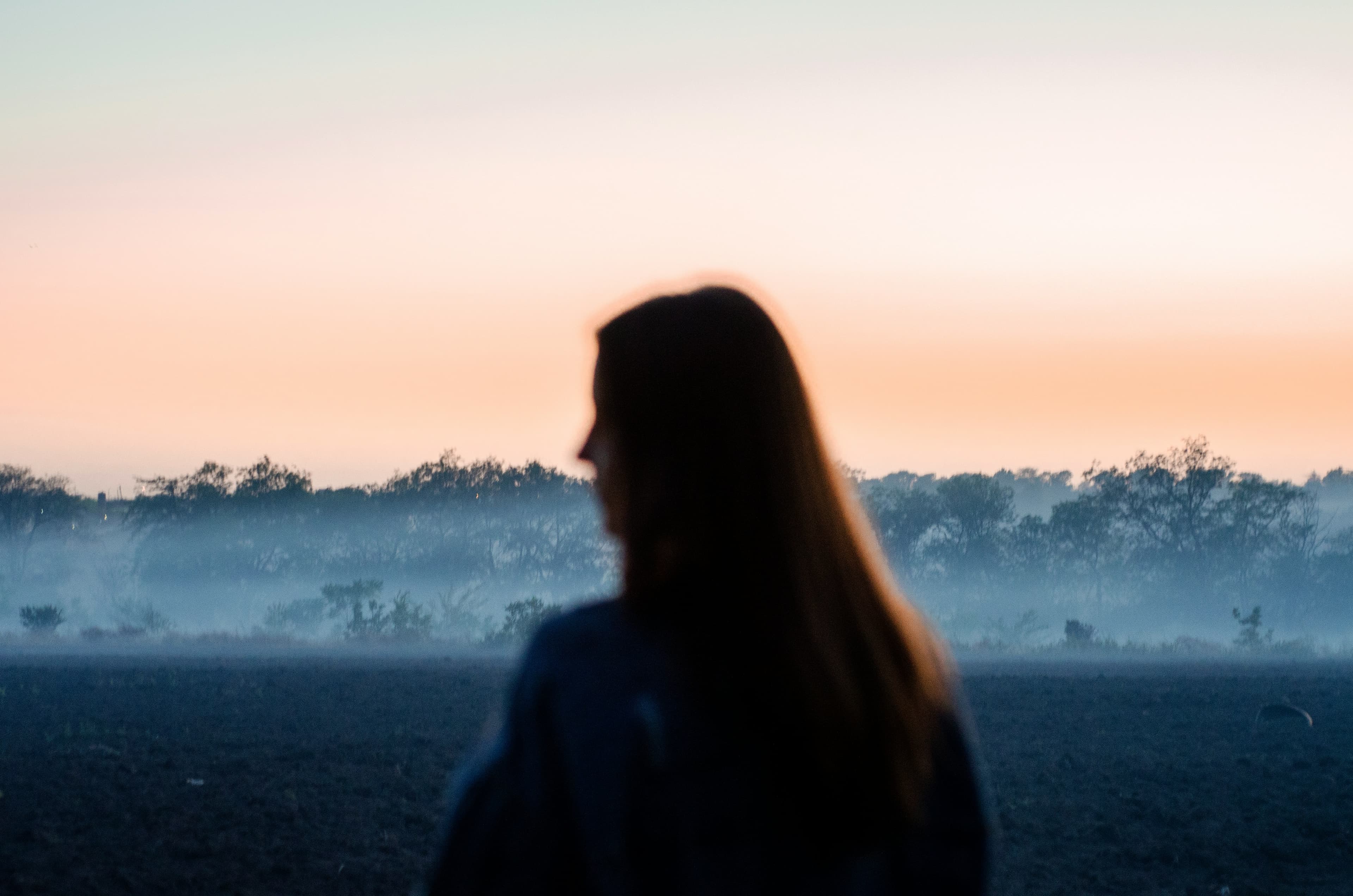 Mujer mirando el horizonte desde una ventana, con una taza entre las manos y la luz de la tarde entrando suave.